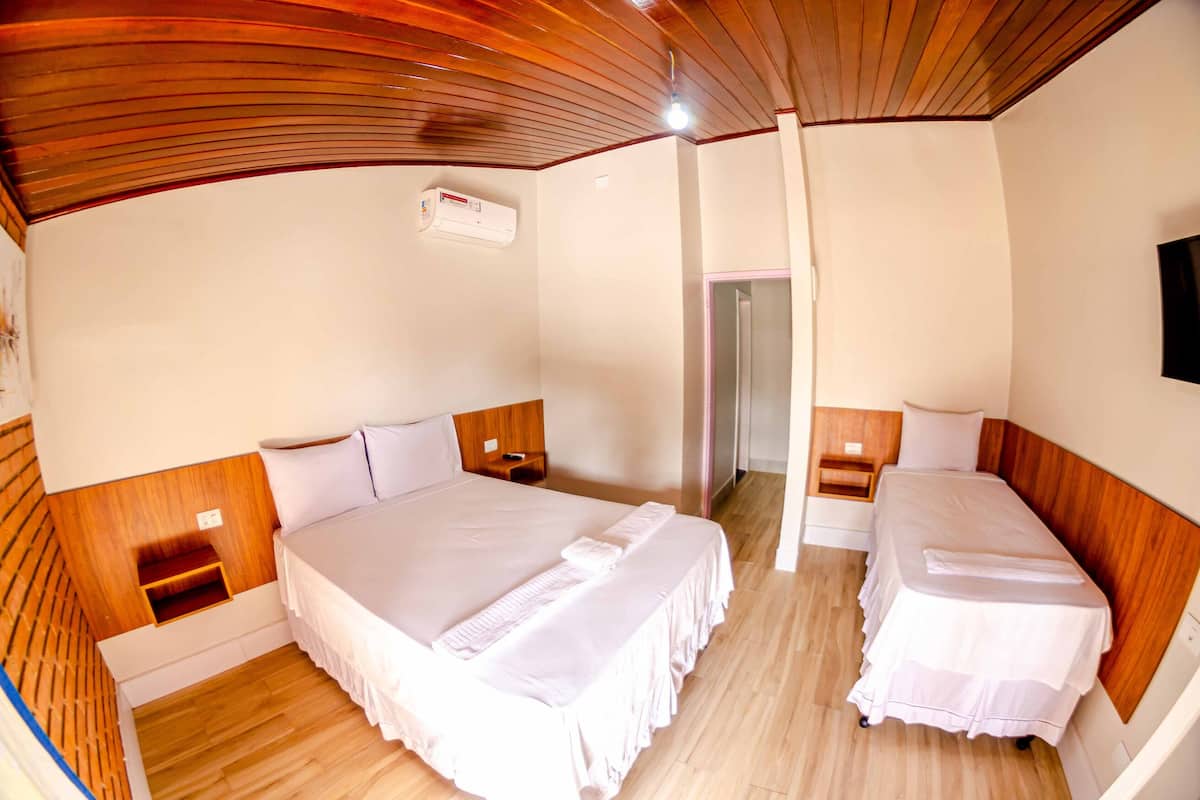 Habitación de hotel con dos camas individuales, cabeceros de madera, ventilador de techo y aire acondicionado de pared.