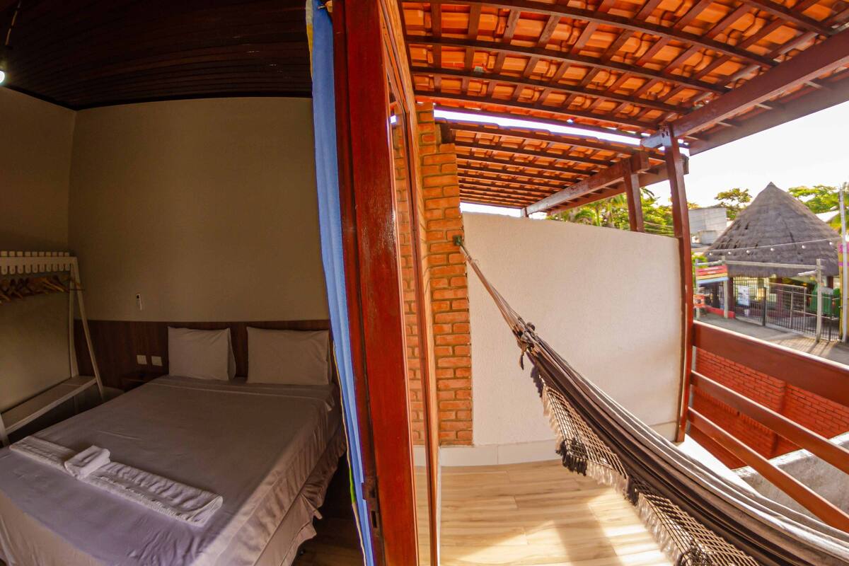 Una habitación con cama, ventana con vista a una construcción de techo de paja y techo de madera.