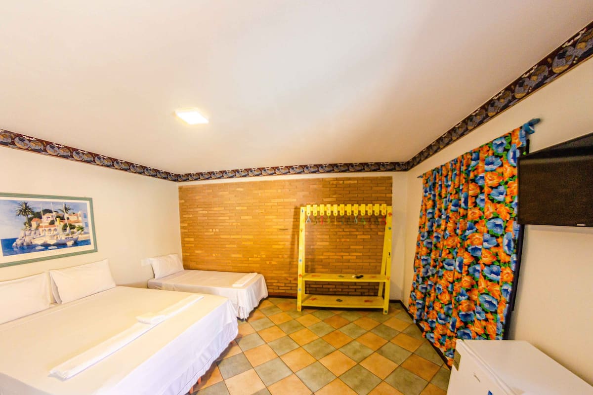 Habitación de hotel con dos camas individuales, un banco de madera, una cortina colorida, un cuadro en la pared y suelo de baldosas.