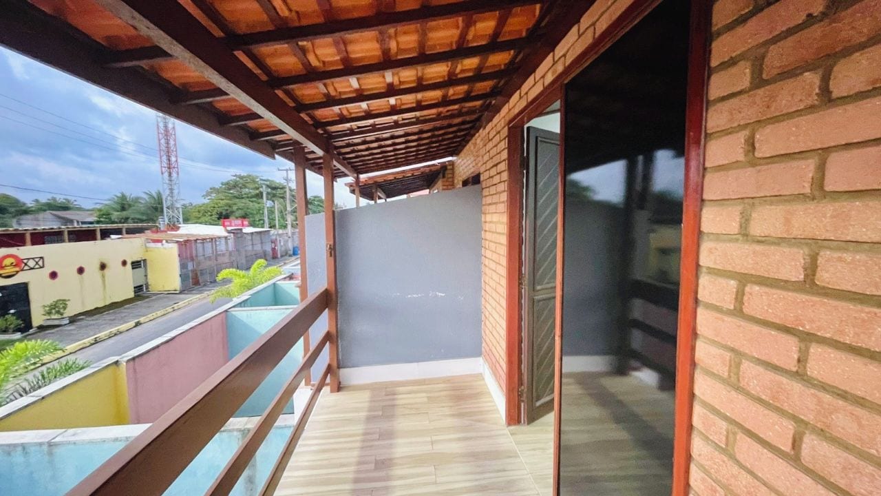 A balcony with a wooden floor, a glass door, and a view of a street with buildings and a power line tower.