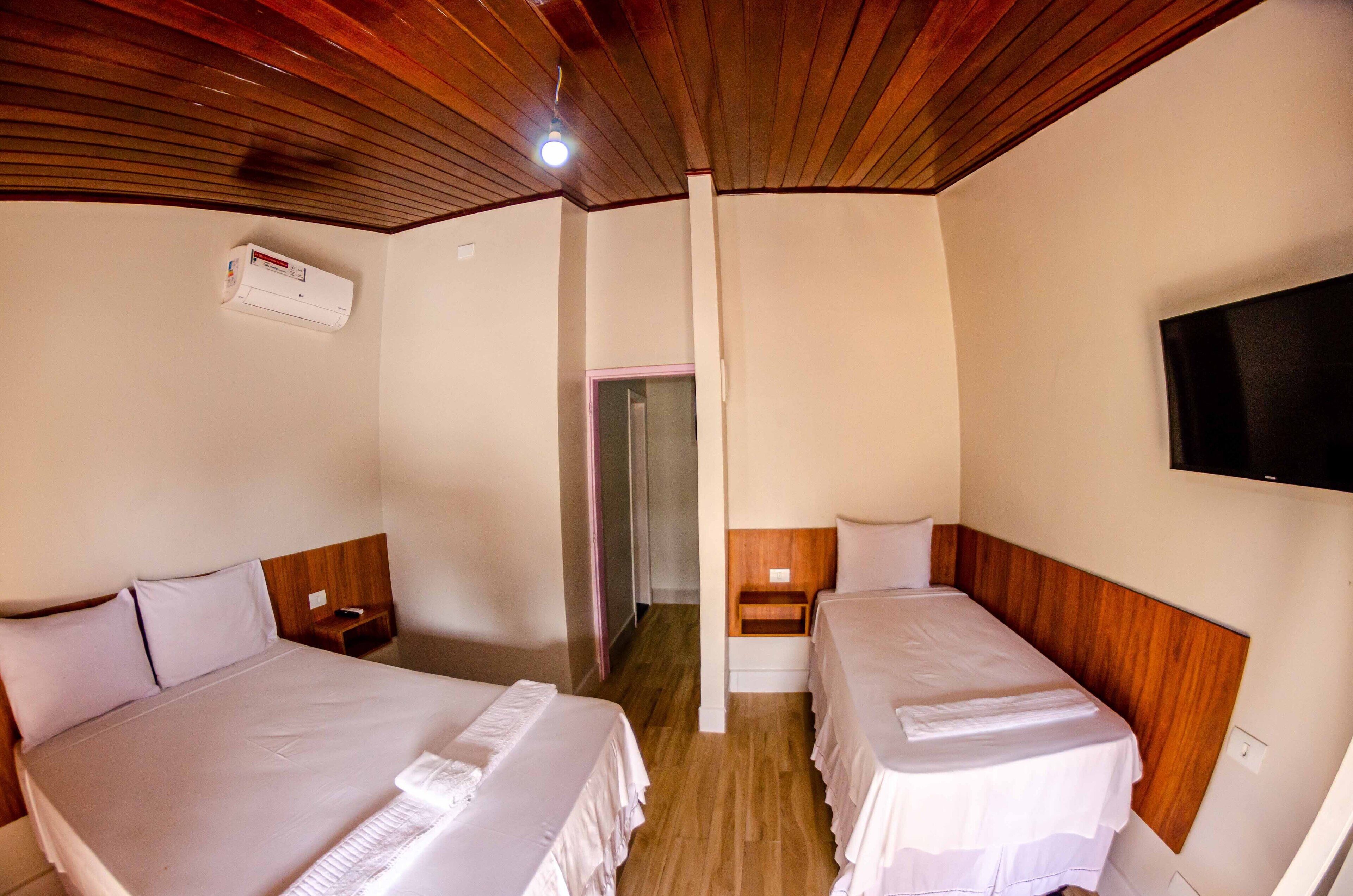 A hotel room with two beds, wooden headboards, a flat-screen TV mounted on the wall, and an air conditioning unit on the wall.