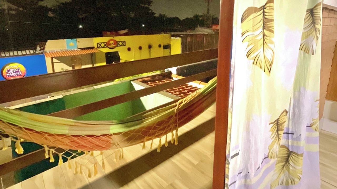 A hammock on a balcony with a view of a building and a restaurant in the background.