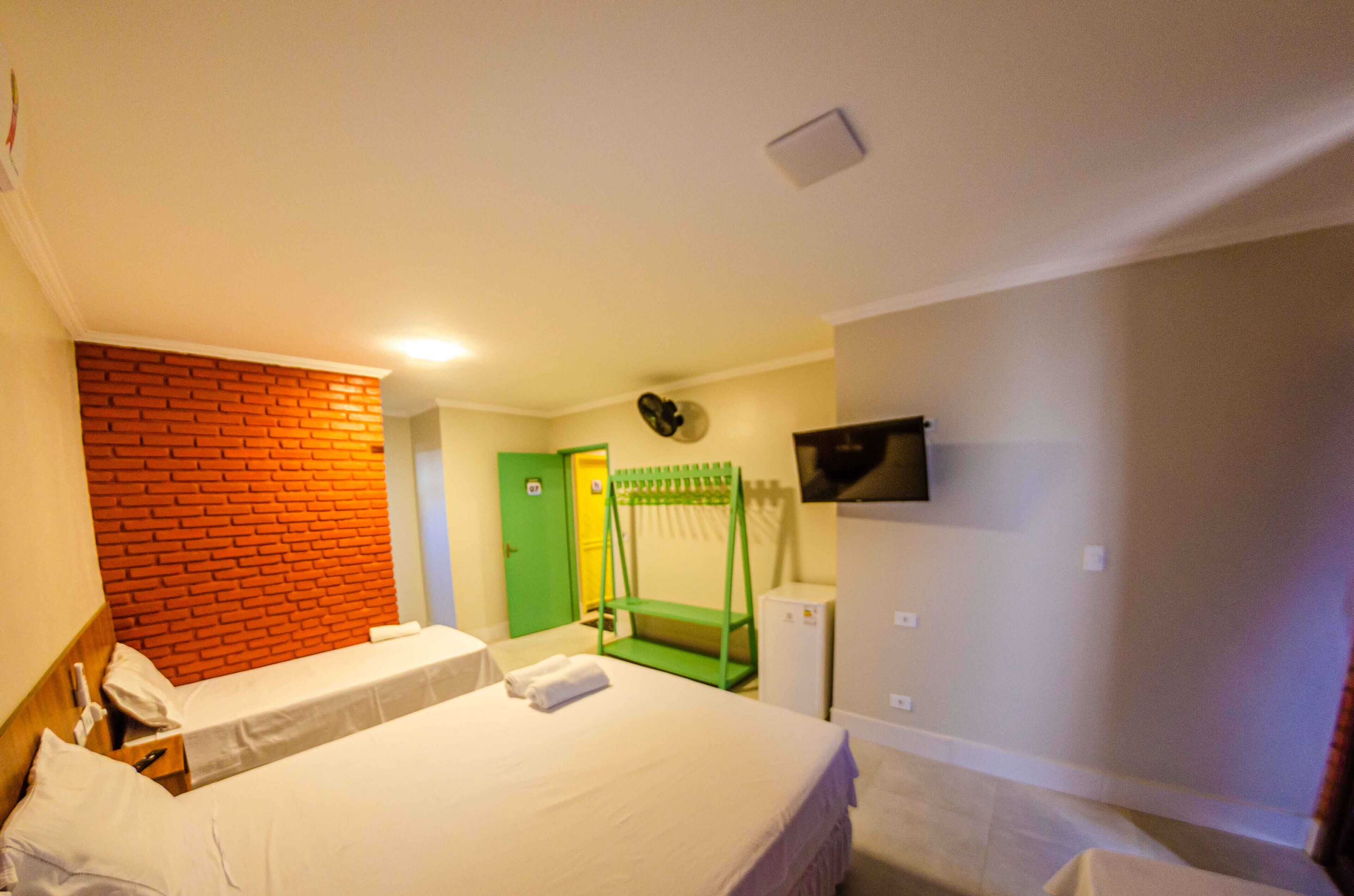 A hotel room with two beds, a green door, a TV on the wall, and a brick accent wall.