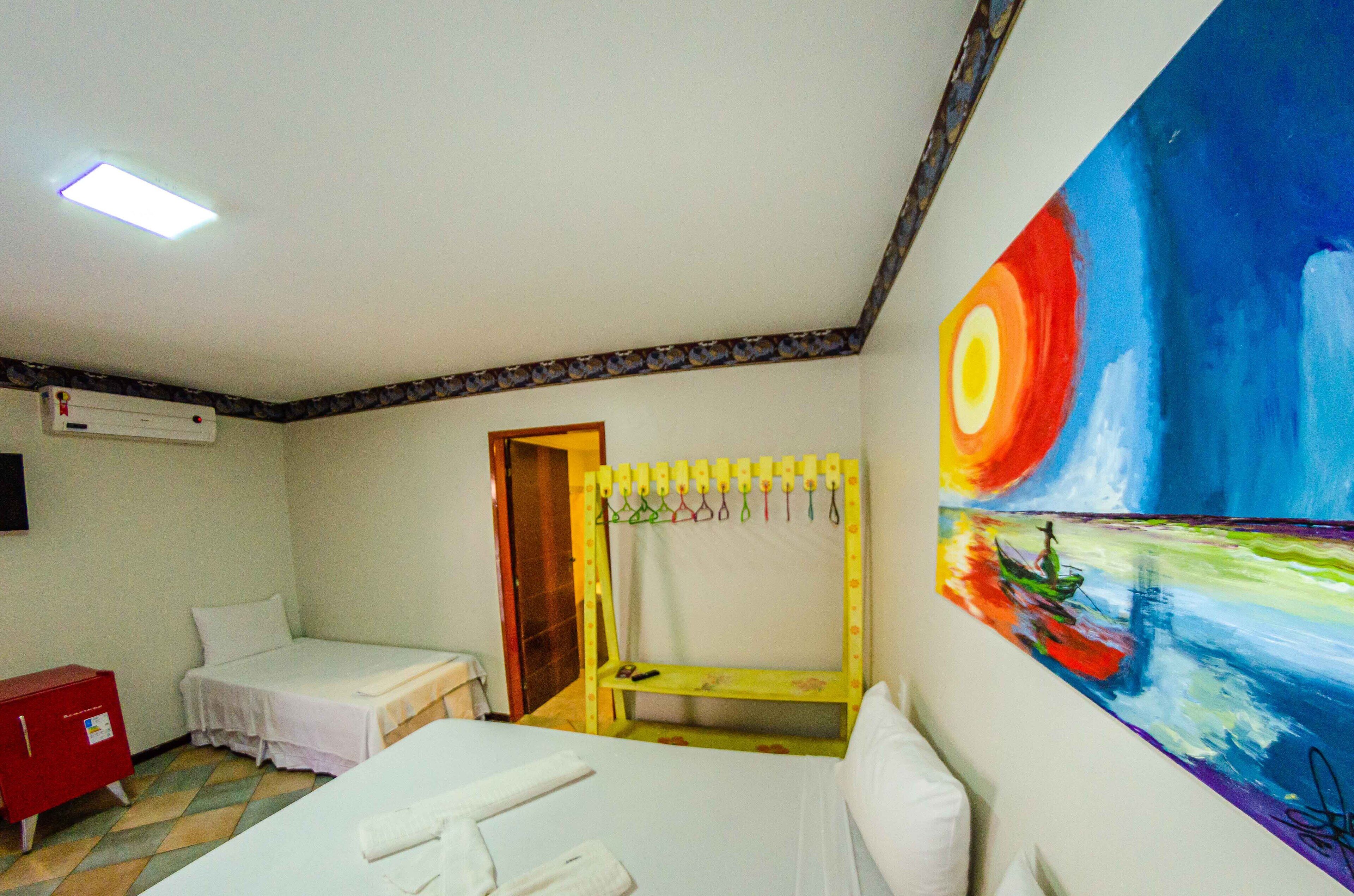 Una habitación con una cama, un banco, un armario rojo y un cuadro en la pared.