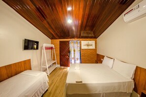 Habitación de hotel con dos camas, techo de madera, paredes blancas y una pared de ladrillo.