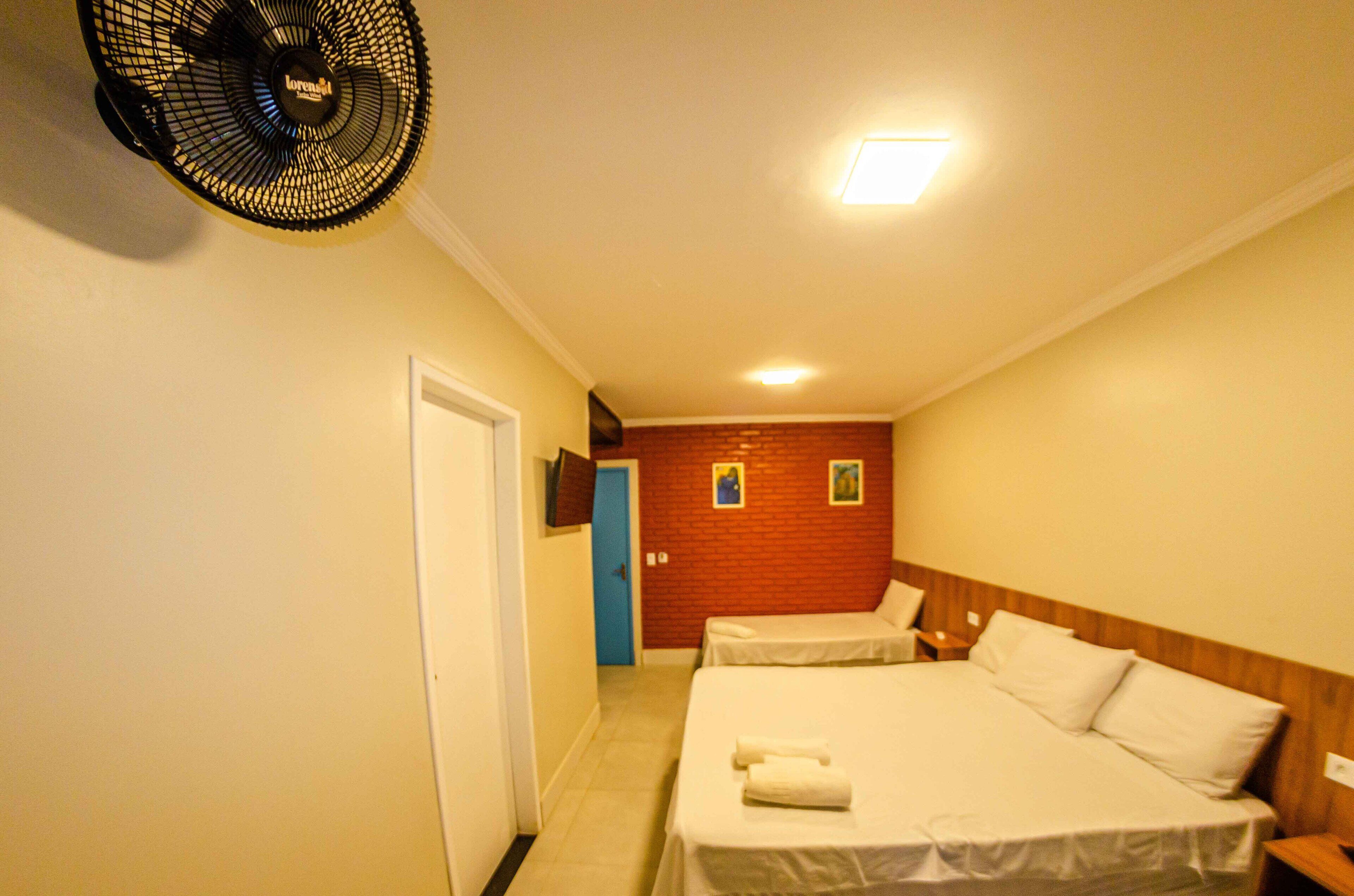 A hotel room with two beds, a ceiling fan, a door, and a red brick wall.