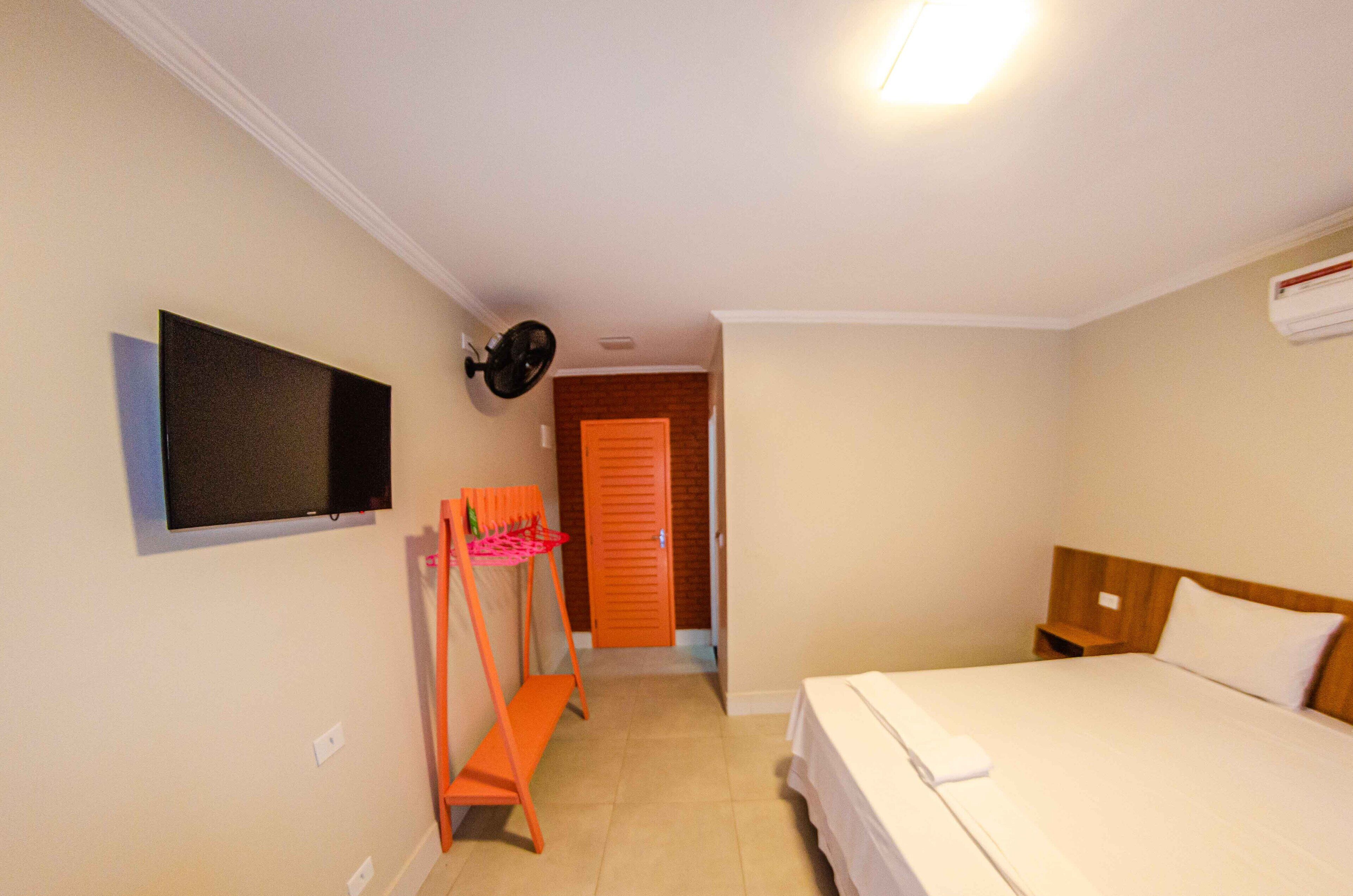A hotel room with a bed, a TV mounted on the wall, a fan, and a wooden headboard.