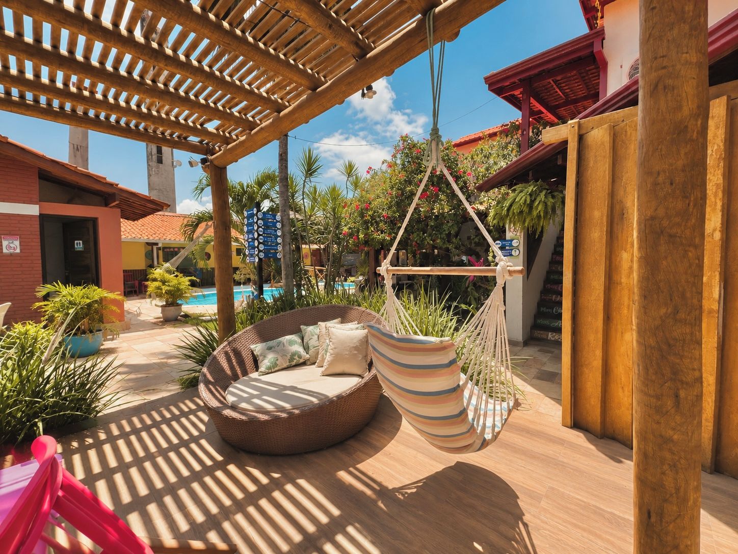 Un área junto a la piscina con una silla colgante, una hamaca y un pérgola de madera.