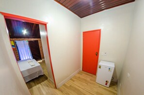 Una habitación pequeña con piso de madera, una puerta blanca y un refrigerador blanco.