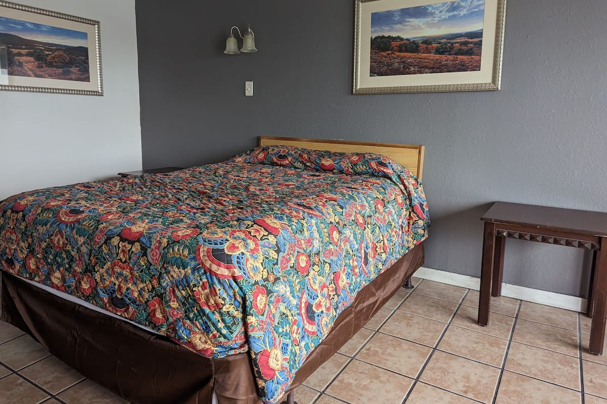 Una camera da letto con un letto, un comodino, due luci a parete e due quadri con paesaggi.