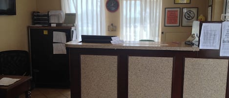 Uma receção com um relógio, um computador e uma janela com cortinas.