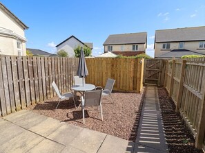 A backyard with a wooden fence, a patio table with chairs, and a gravel area. - Ahoy (Seahouses)