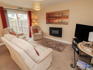 A living room with two reclining chairs, a television, a fireplace, and a view of the outside. - Ahoy (Seahouses)