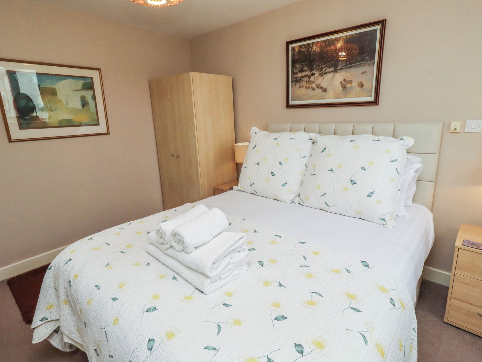 A bedroom with a bed, a wardrobe, a nightstand, and two framed pictures on the wall.