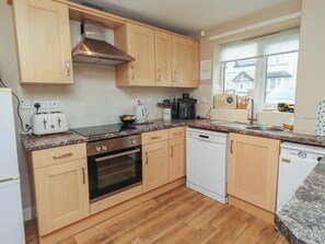 A kitchen with wooden cabinets, a stainless steel range hood, a toaster, a coffee maker, a dishwasher, and a window with a view of a house.