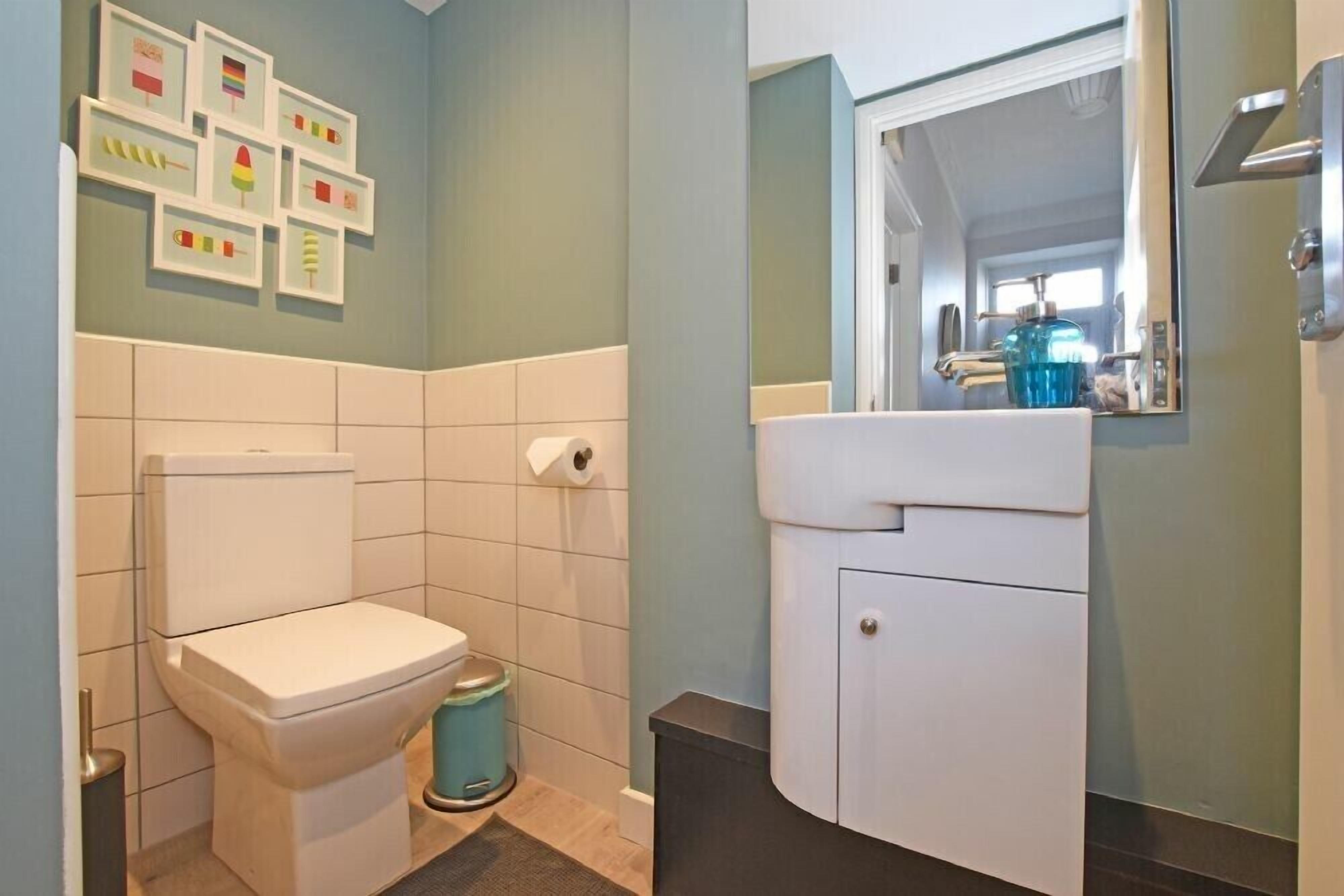 Un baño con inodoro, lavabo y espejo. Hay cuadros enmarcados en la pared.