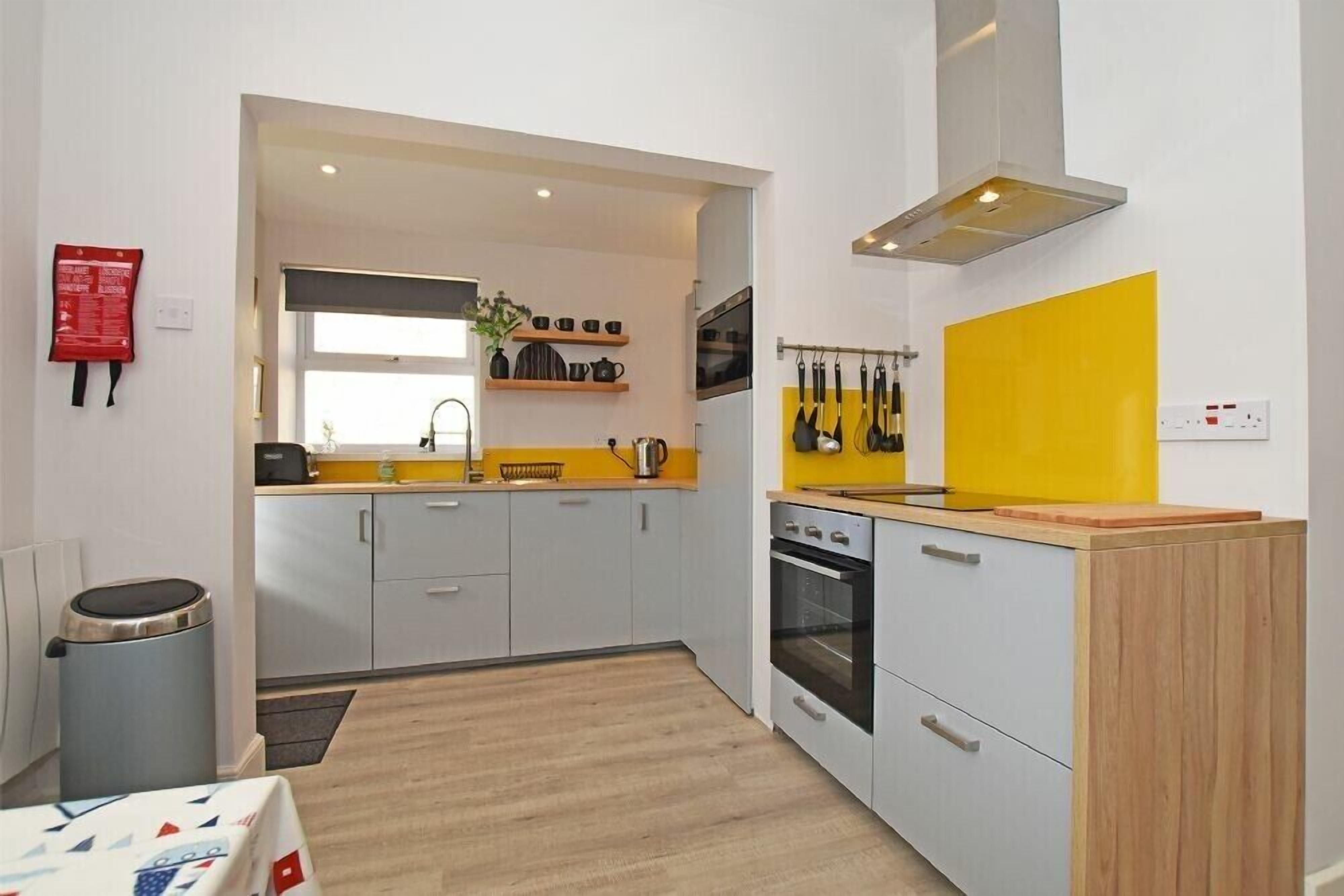 A compact kitchen with grey cabinets, a yellow backsplash, and a stainless steel range hood.