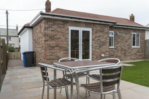 Une maison en briques avec un toit en tuiles, une terrasse avec une table et des chaises, et un petit jardin.