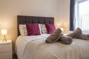 Un lit bien fait, avec une couvre-lit à rayures et deux oreillers, une lampe de chevet et une fenêtre avec des rideaux.
