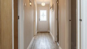 A narrow hallway with a wooden floor, a white door at the end, and a small window with a decorative design. - Southfield Lodge (Seahouses)