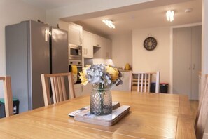 Un coin repas avec une table en bois, des chaises, un vase de fleurs et, au fond, une cuisine.