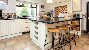 A kitchen with a large island, bar stools, a microwave, and a view of the outdoors. - Aryarch (Alnwick)