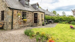 A stone house with a sloped roof, a front door, and a patio area with outdoor furniture. - Aryarch (Alnwick)