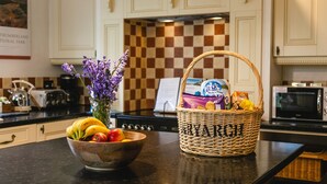 A kitchen with a checkered backsplash, a stove, a microwave, a toaster, and a bowl of fruit and a basket of groceries on the counter. - Aryarch (Alnwick)