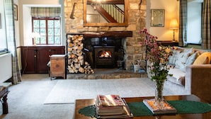 A cozy living room with a stone fireplace, a wooden staircase, a sofa, and a coffee table with magazines. - Aryarch (Alnwick)