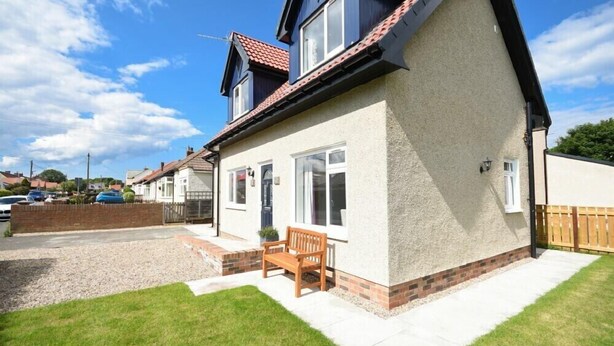 A two-story house with a sloped roof, a front porch with a bench, and a well-maintained lawn. - The Chevy (Seahouses)