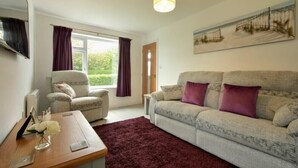 A living room with a grey sofa, two armchairs, a wooden coffee table, and a large window with purple curtains. - The Chevy (Seahouses)