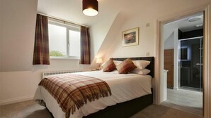 A bedroom with a bed, a window with curtains, a bedside lamp, and a door leading to a bathroom. - The Chevy (Seahouses)