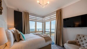 Camera d'albergo con un letto grande, una sedia, un televisore e vista mare attraverso ampie finestre.