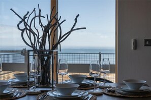 A dining table set with white plates, bowls, and wine glasses, with a view of the sea through a window. - Keildon (Seahouses)