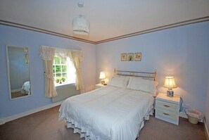 A bedroom with a large bed, two bedside tables with lamps, a mirror, and a window with curtains.