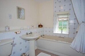 A bathroom with a toilet, sink, and bathtub. There is a window with a plant on the windowsill.