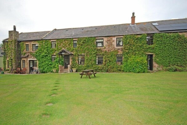A stone building with ivy covering the walls, a front door, and a picnic table in the yard.