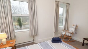 Quarto de hotel com duas camas, uma cadeira de balanço, uma mesinha com abajur e vista para o exterior pela janela.