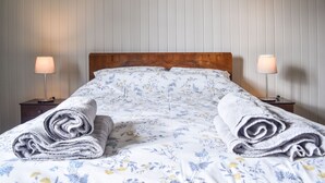 A neatly made bed with floral bedding, two bedside lamps, and rolled towels on the side. - Garden House (Alnwick)