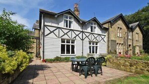 A traditional house with a stone facade, a tiled patio with outdoor furniture, and a garden with flowers and shrubs. - Garden House (Alnwick)