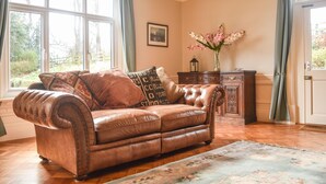 A room with a leather sofa, a wooden cabinet, a framed picture on the wall, and a window with curtains. - Garden House (Alnwick)