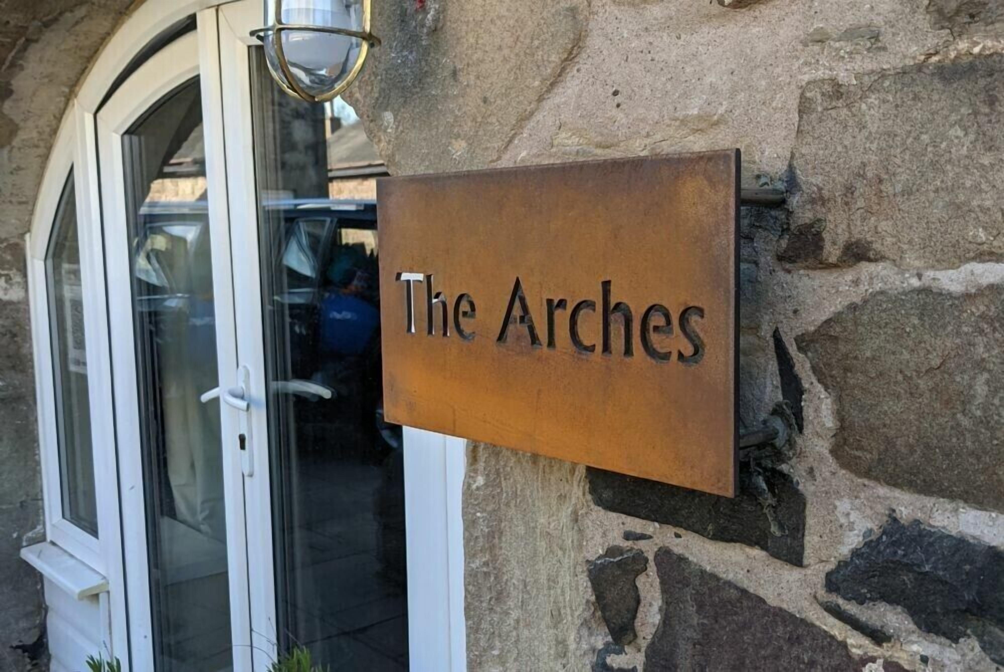 A sign reading "The Arches" mounted on a stone wall.
