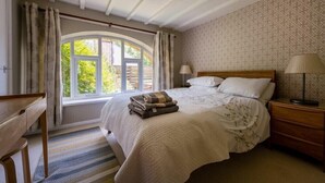 Una camera da letto con un'ampia finestra, un letto con copripiumino floreale, un comodino con una lampada e una scrivania in legno.