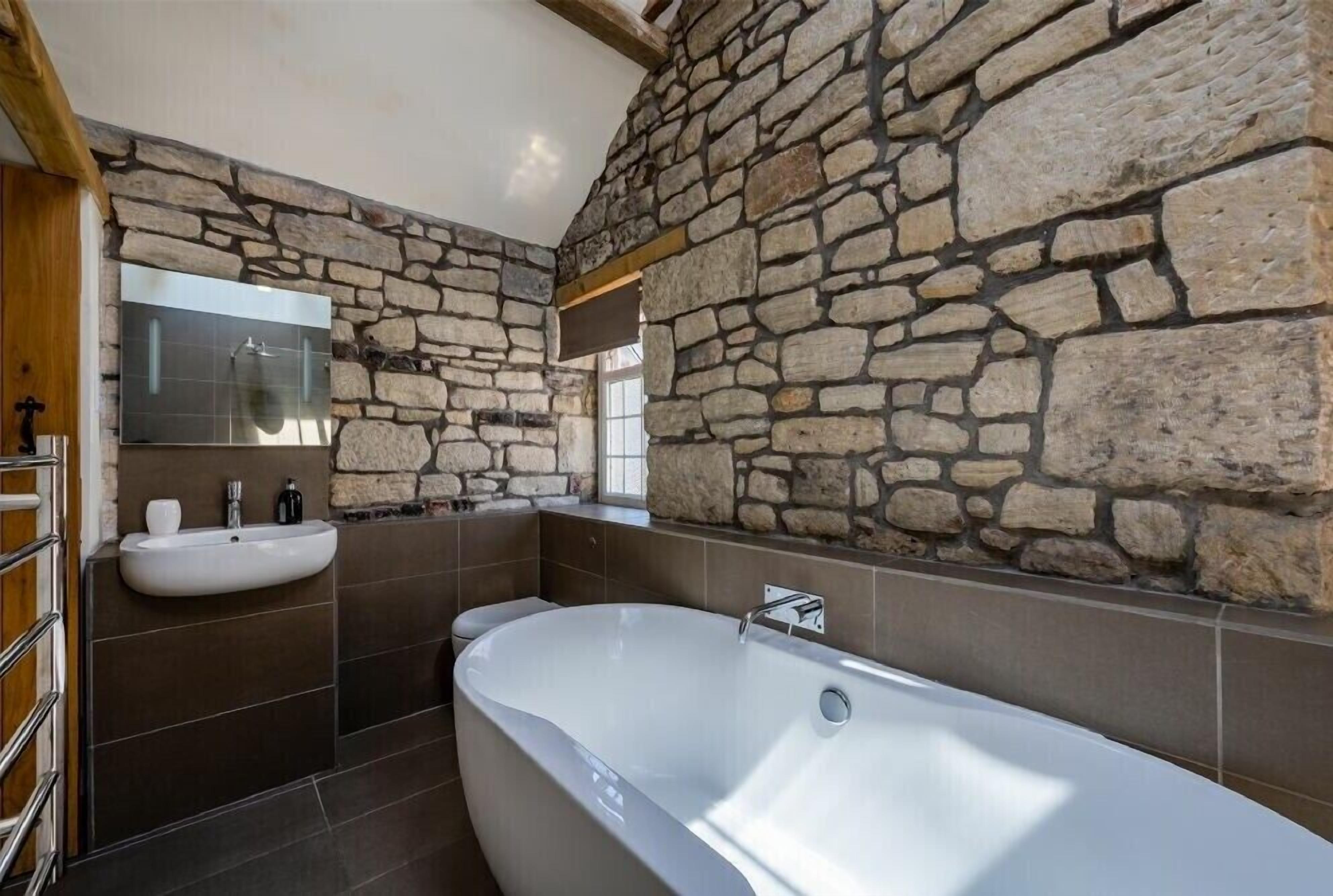 A bathroom with stone walls, a bathtub, and two sinks.