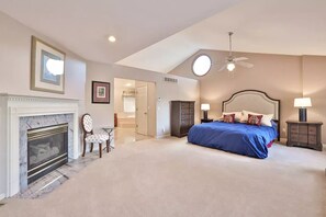 Relax in this serene bedroom with a large bed, fireplace, and ceiling fan.