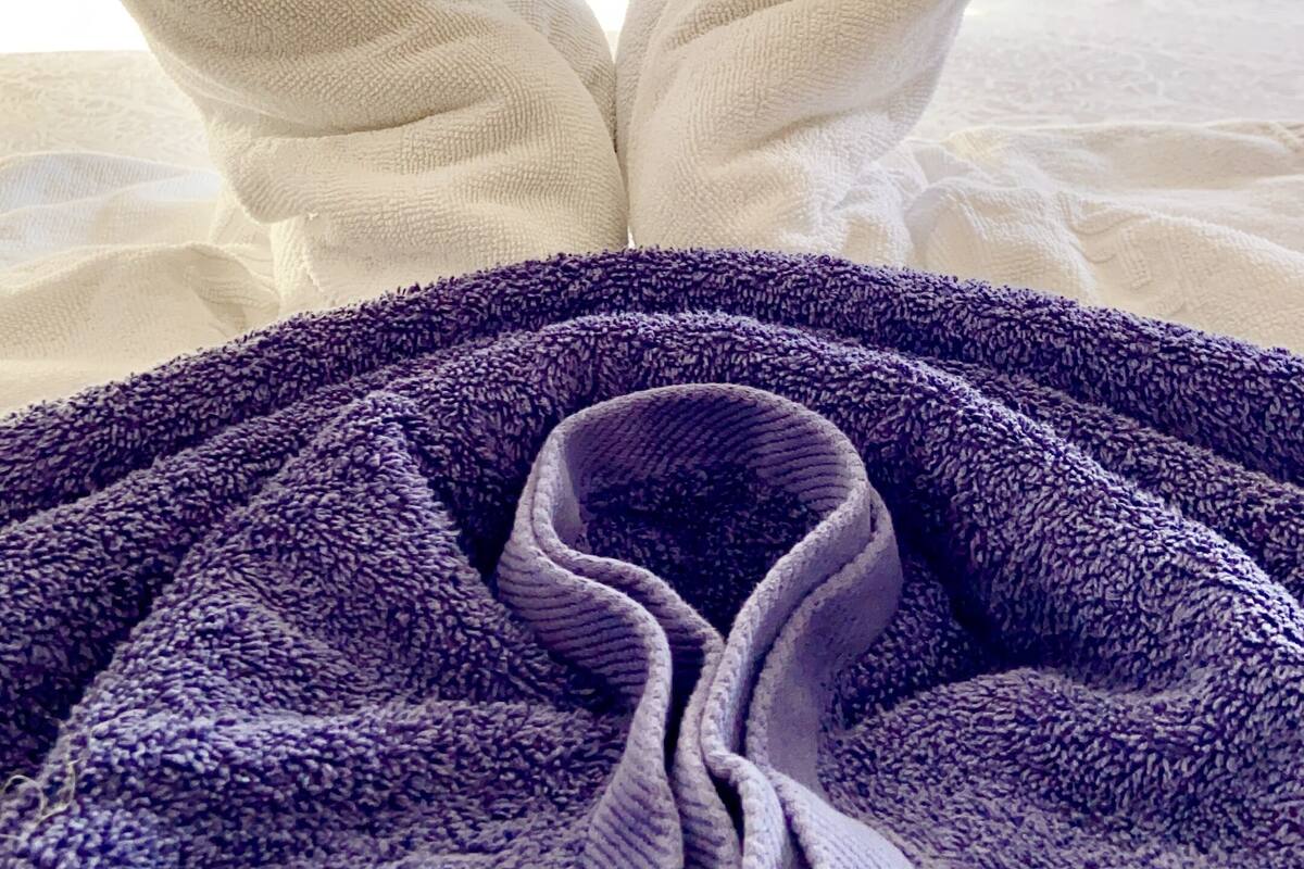 Un lit avec une serviette pliée en forme de cœur et une couverture violette.