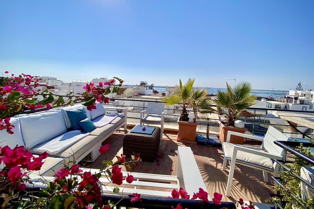 Une terrasse sur le toit, avec des chaises longues blanches, une petite table et des plantes en pot.