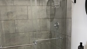 Un box de ducha moderno con puerta de vidrio, un lavamanos blanco y un perchero para toallas.