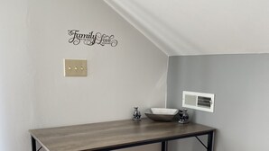 Una cocina con una mesa de madera y dos taburetes, un interruptor de luz en la pared y una rejilla de ventilación.