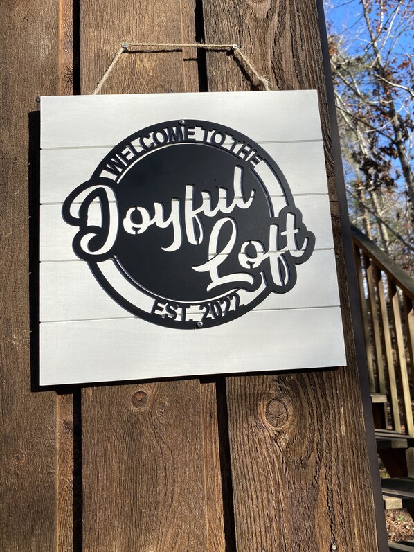 A sign with the text "Welcome to the Joyful Loft" and "EST. 2017" on a wooden background.